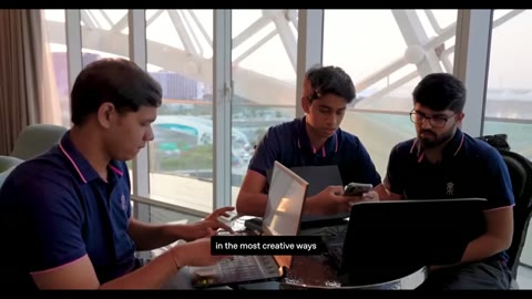 Source frame at 145.500s. Interview, student laptop groups, and glass-walled presentation room.