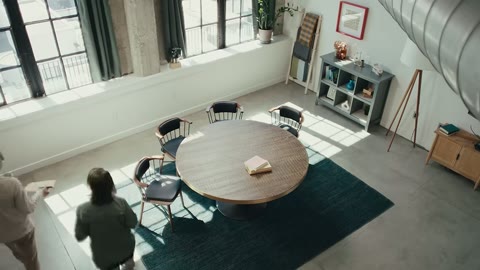 Source frame at 0.500s. Overhead meeting room, arrivals, seated conversation.