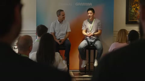 Source frame at 20.500s. Panel seating, interview closeup and attendee conversation.